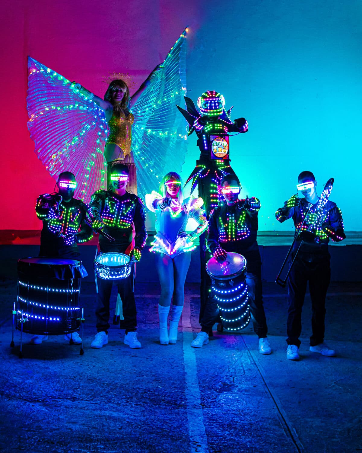 Batucada LED alongside stilt walkers with illuminated wings and an LED robot