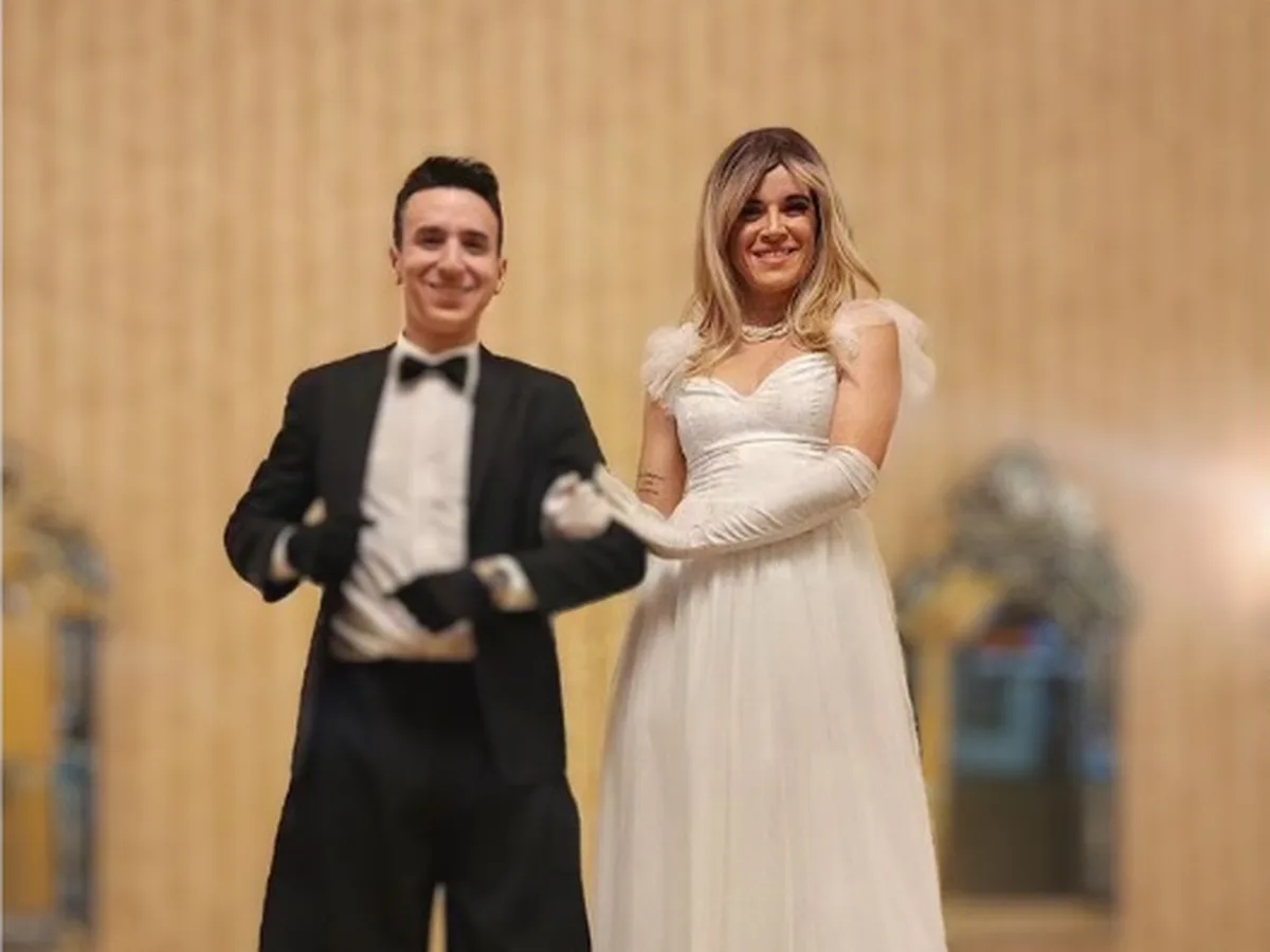 Novios en zancos con esmoquin negro y vestido blanco en un salón