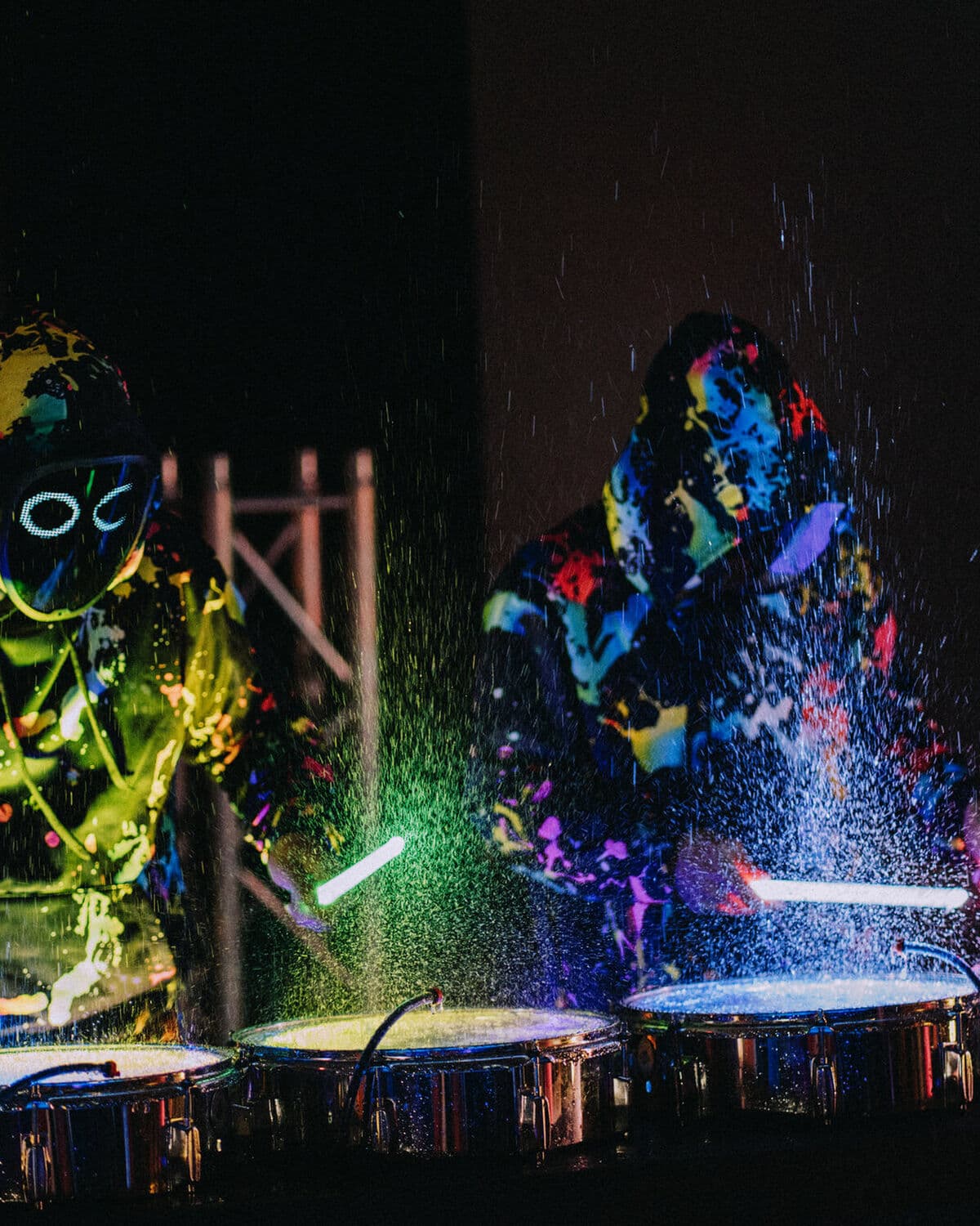 Dos percusionistas de Splash Drummers con trajes fluorescentes y baquetas de luz