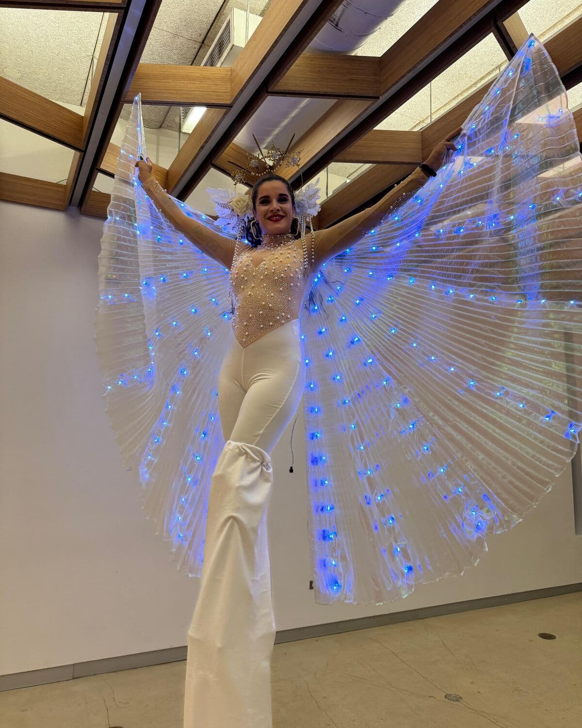Zanquera con alas de luz blanca y tocado de plumas en un salón